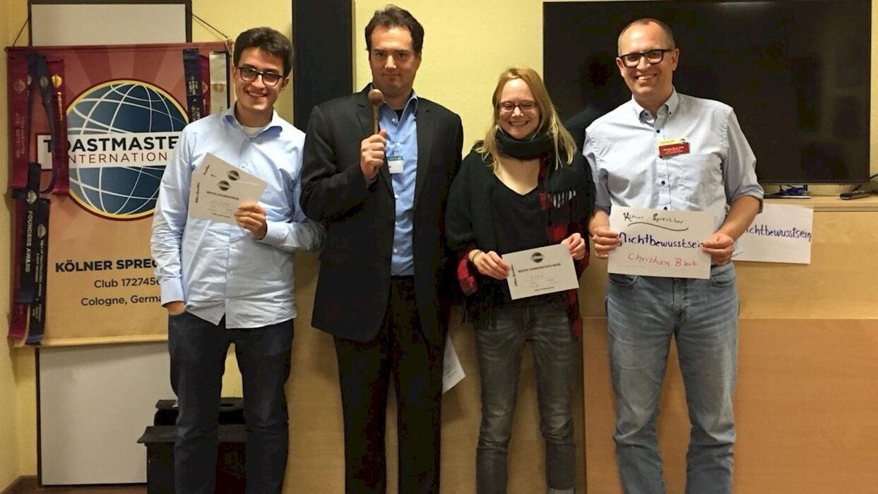 Vier Teilnehmende stehen mit Urkunden und Hammer vor dem Toastmasters-Banner.