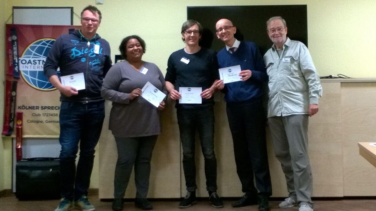 Fünf Mitglieder der Kölner Sprechbar mit Urkunden vor dem Toastmasters-Banner.