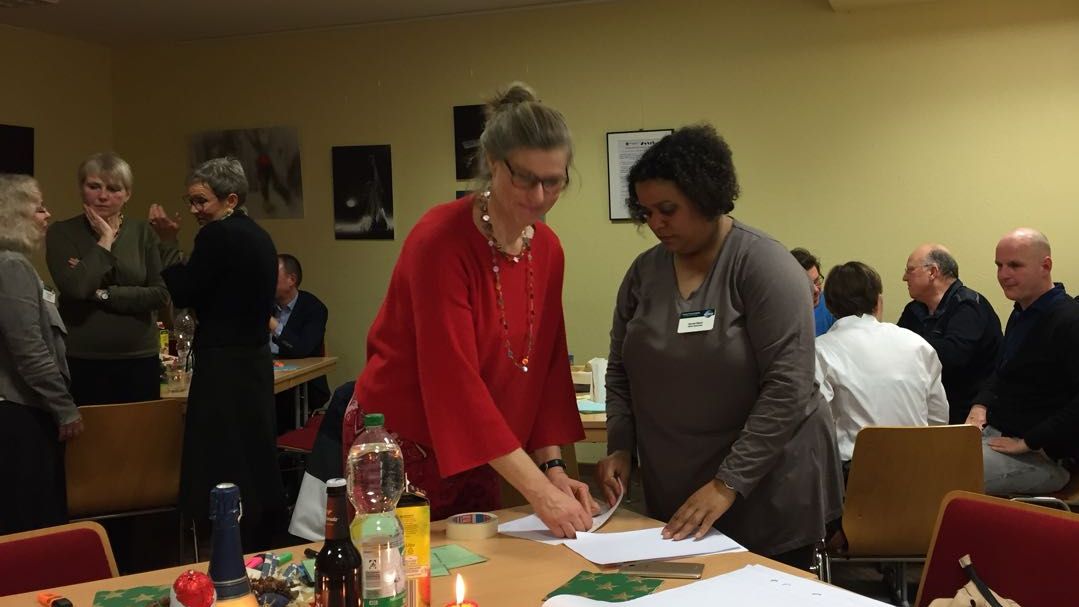 Norvisi und Claudia, die Moderatorinnen des Abends, bereiten am Tisch die Weihnachtsfeier der Kölner Sprechbar vor, im Hintergrund weitere Mitglieder.
