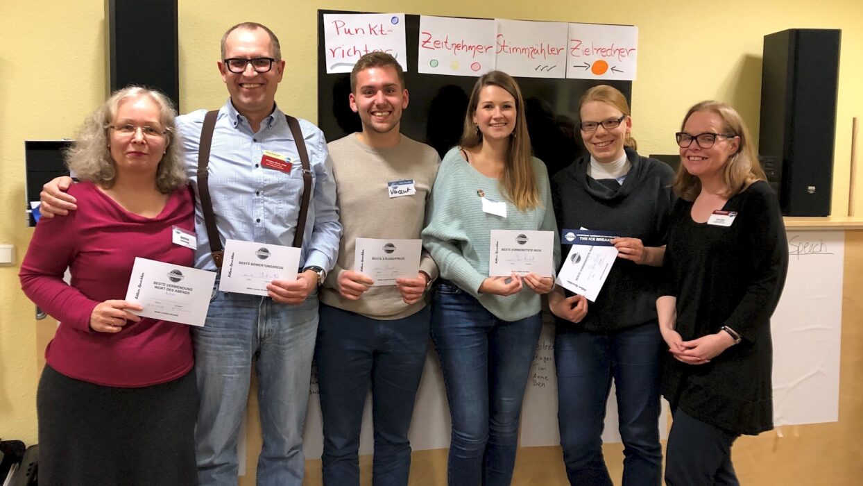 Sechs Teilnehmende stehen mit Urkunden vor Plakaten zu Meeting-Rollen.