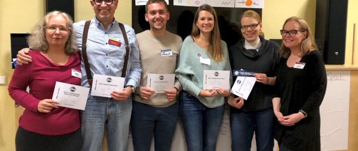 Sechs Teilnehmende stehen mit Urkunden vor Plakaten zu Meeting-Rollen.
