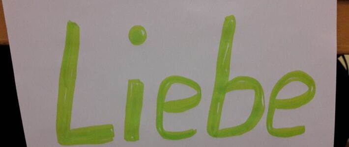 Handgeschriebenes Wort „Liebe“ in grüner Schrift auf einem weißen Blatt Papier.