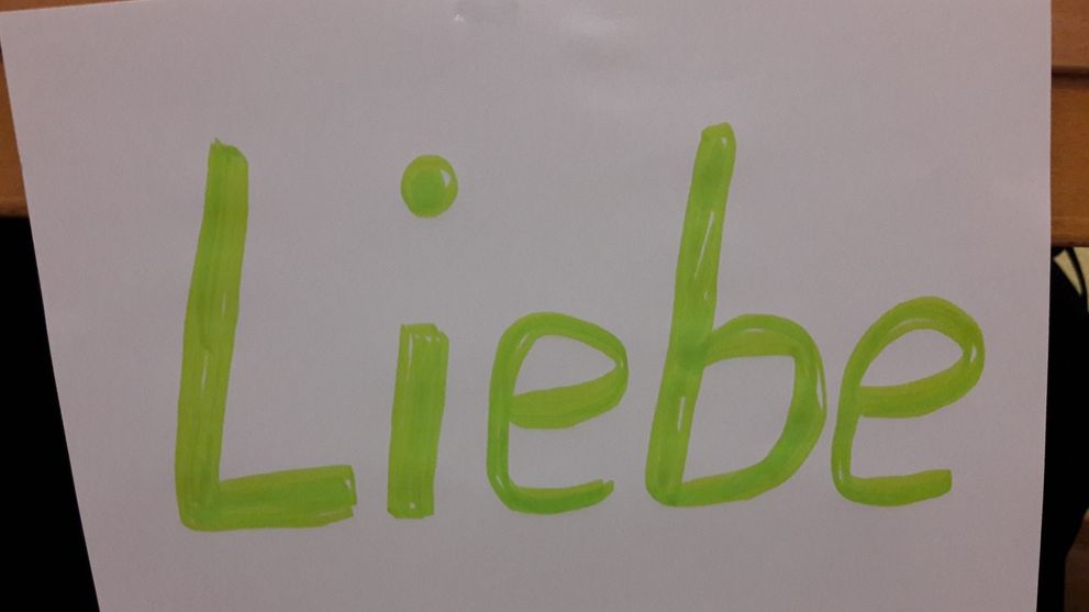 Handgeschriebenes Wort „Liebe“ in grüner Schrift auf einem weißen Blatt Papier.