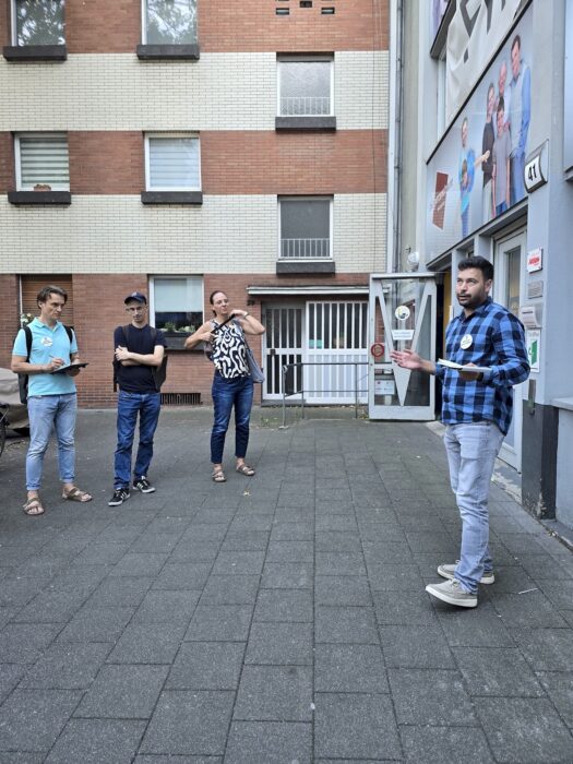 Ein Redner spricht mit ausgestreckter Hand vor dem Eingang des Bürgerzentrums, drei Zuhörende stehen ihm gegenüber.