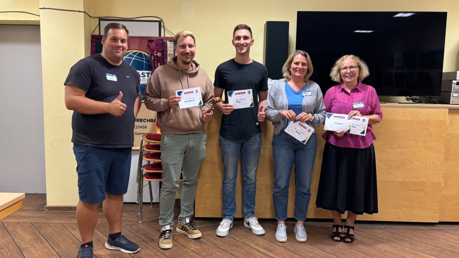 Fünf Teilnehmende stehen mit mehreren Urkunden und einem Rednerhammer im Clubraum der Kölner Sprechbar.