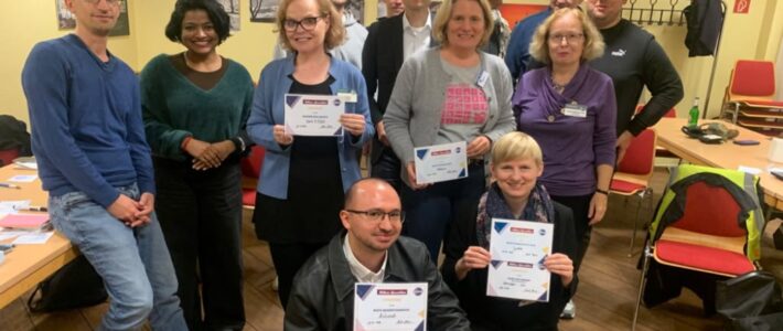 Mut trotz Lampenfieber: Stegreifreden zum Thema Angst Gruppenfoto in einem Seminarraum: Etwa zwölf Personen stehen und knien dicht beieinander, mehrere halten Urkunden in die Kamera. An der gelben Wand im Hintergrund hängen Fotos.